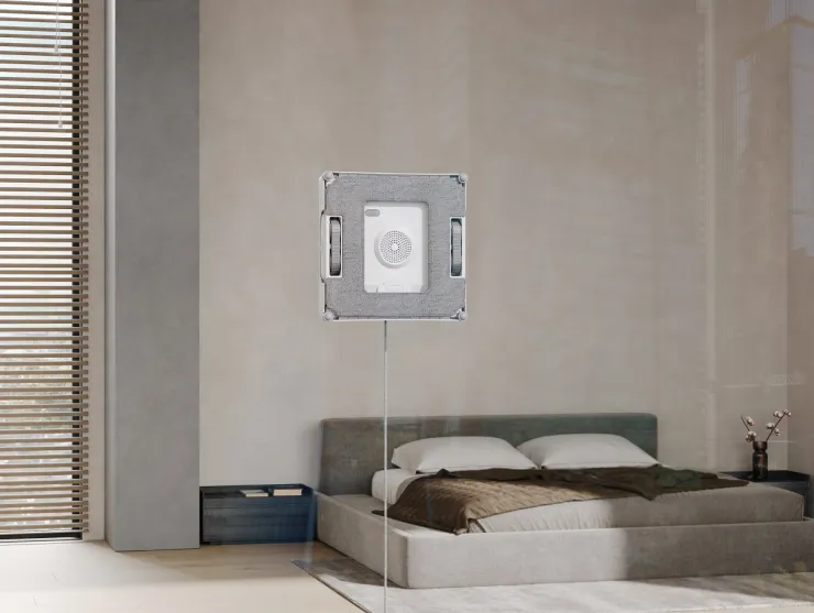 La imagen muestra un limpiador de ventanas robótico de la marca Ecovacs, el modelo WINBOT W2 PRO, colocado en un ambiente moderno y minimalista. Se puede observar el dispositivo en acción, limpiando una ventana en un dormitorio elegante con muebles contemporáneos.
