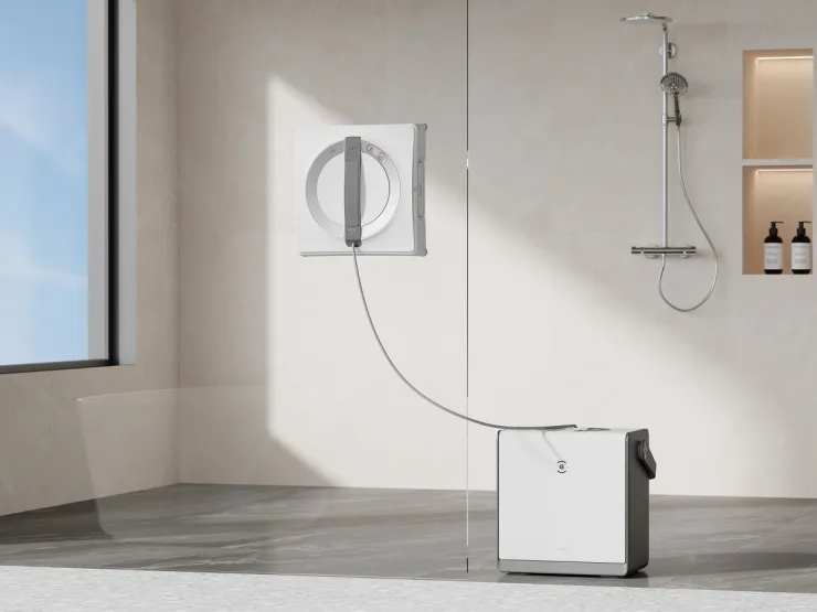La imagen muestra un limpiador de ventanas robótico Ecovacs WINBOT W2 PRO OMNI, instalado en una pared de vidrio en un ambiente moderno y minimalista. El dispositivo está conectado a una base que se encuentra en el suelo, lo que sugiere su uso en la limpieza de ventanas altas o de difícil acceso.